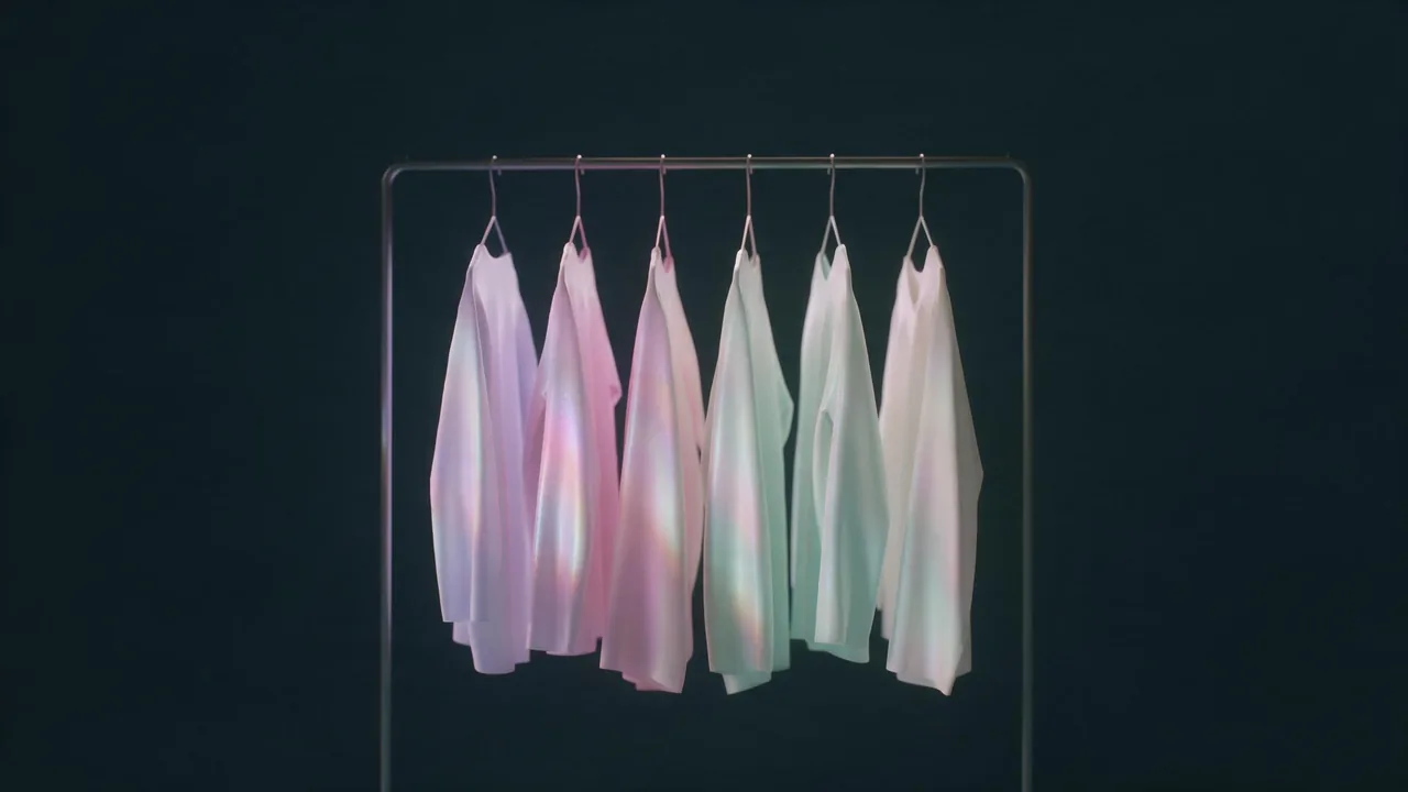 A minimal clothing rail holding six empty garments in pale lilac, rose, mint and ivory against a dark ground